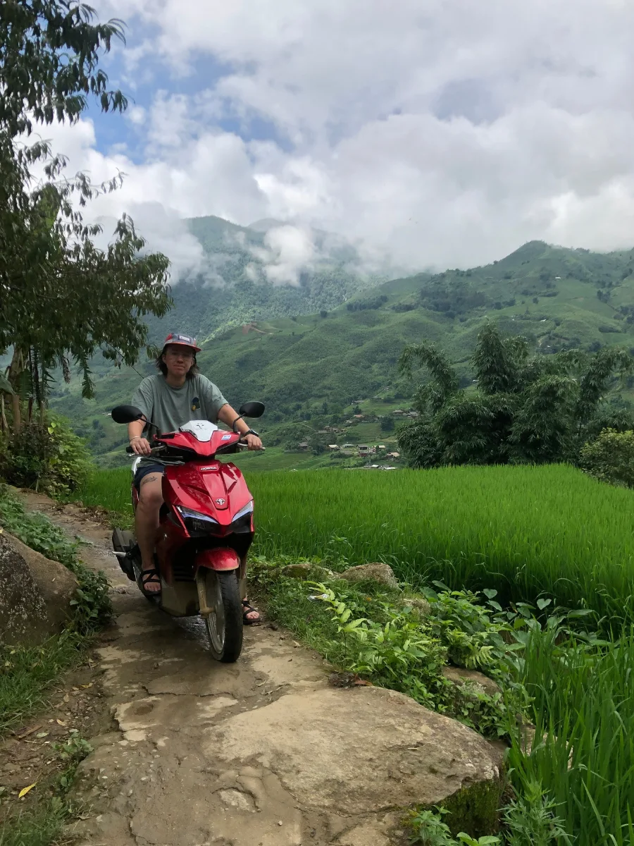 A person riding an automatic motorbike on a small road next to a rice field in Sapa Vietnam