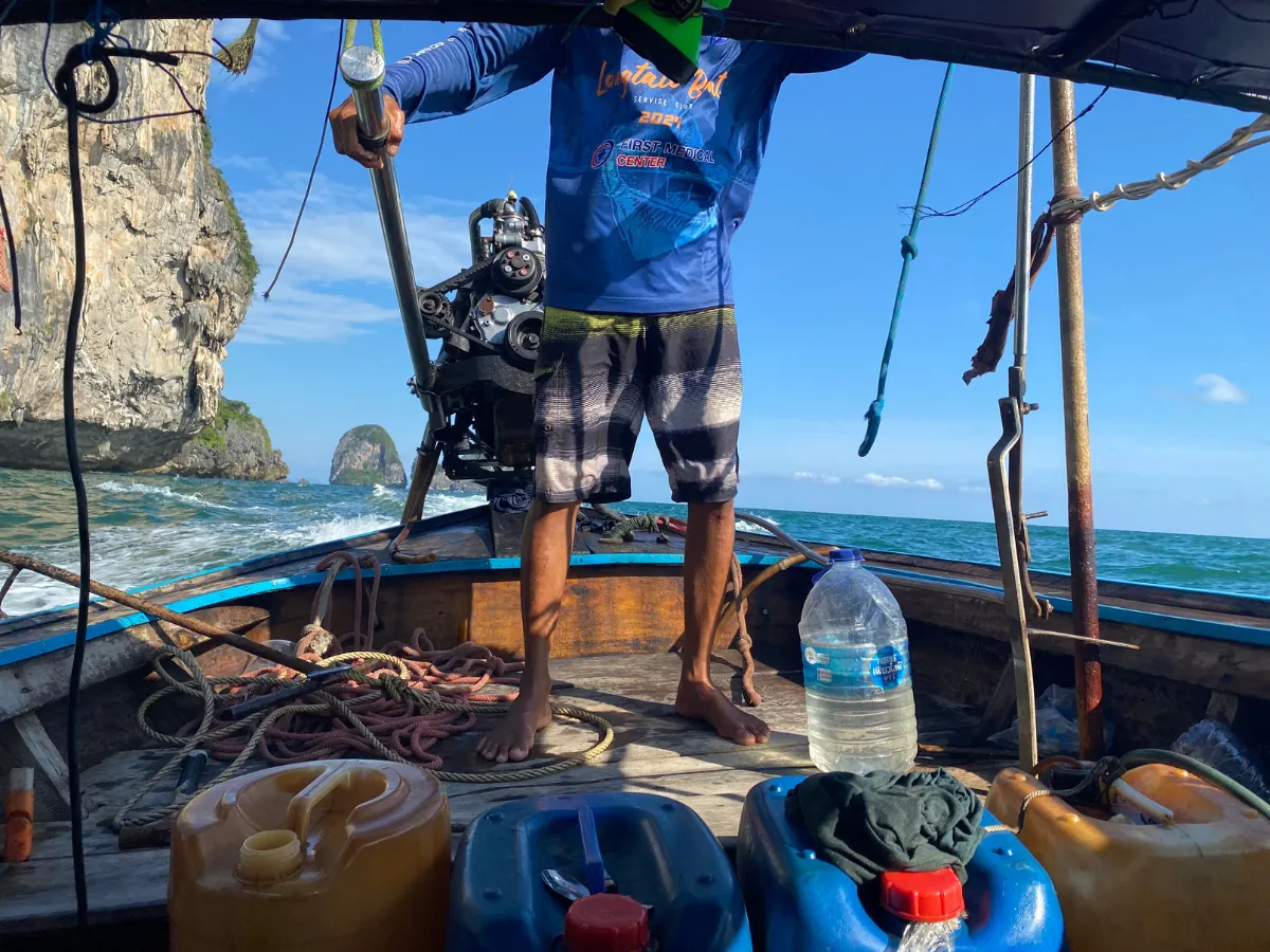 a Thai boat driver standing at the back of a longtail boat heading back to Ao Nang from Railay Beach Lagoon